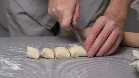 close-up the chef's hands cut strip of dough into pieces and roll them in flour.