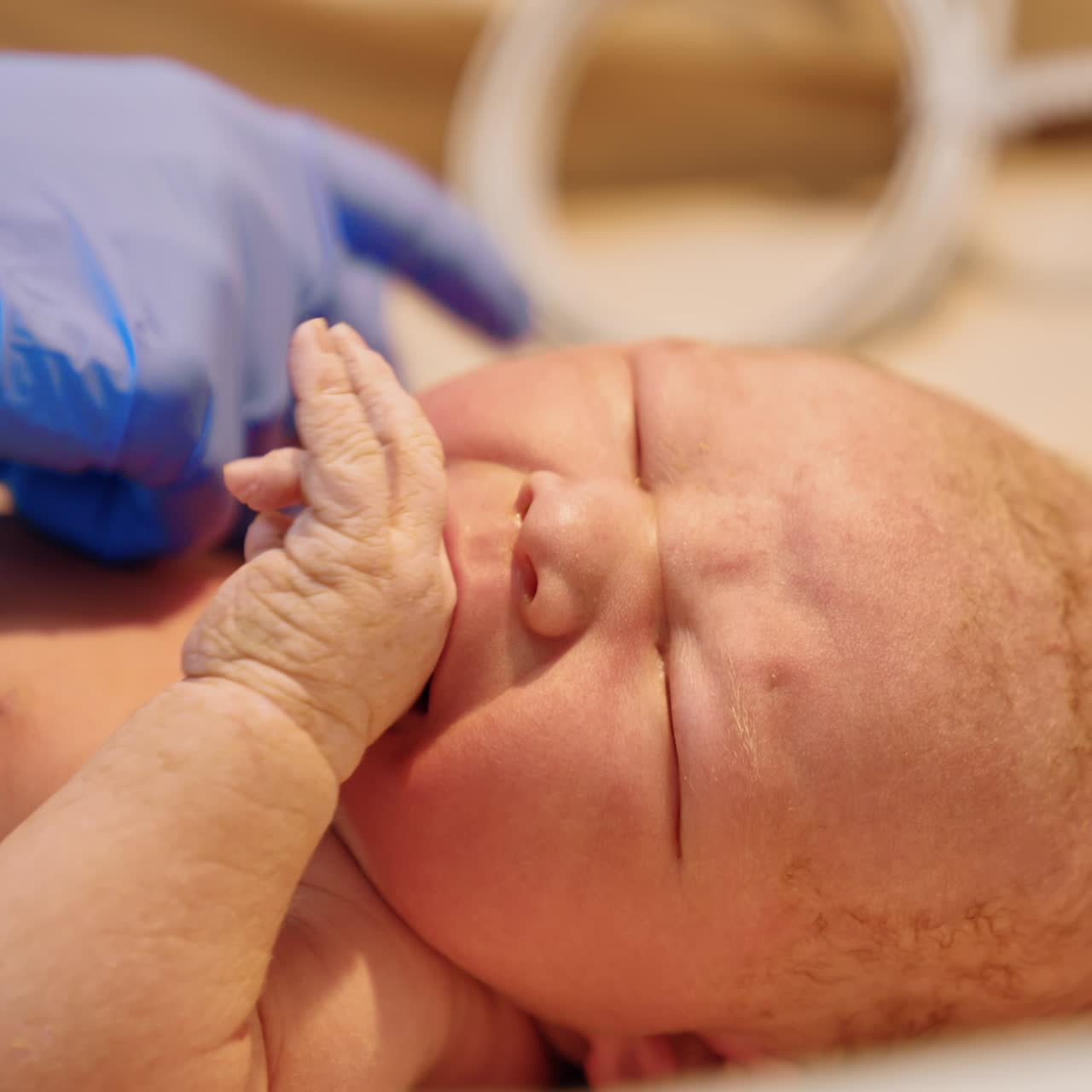 Crying newborn baby on the table. Medic in latex gloves attaches the wire to a child's hand. Close up