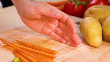 hand slicing carrots with potatoes and peppers nearby