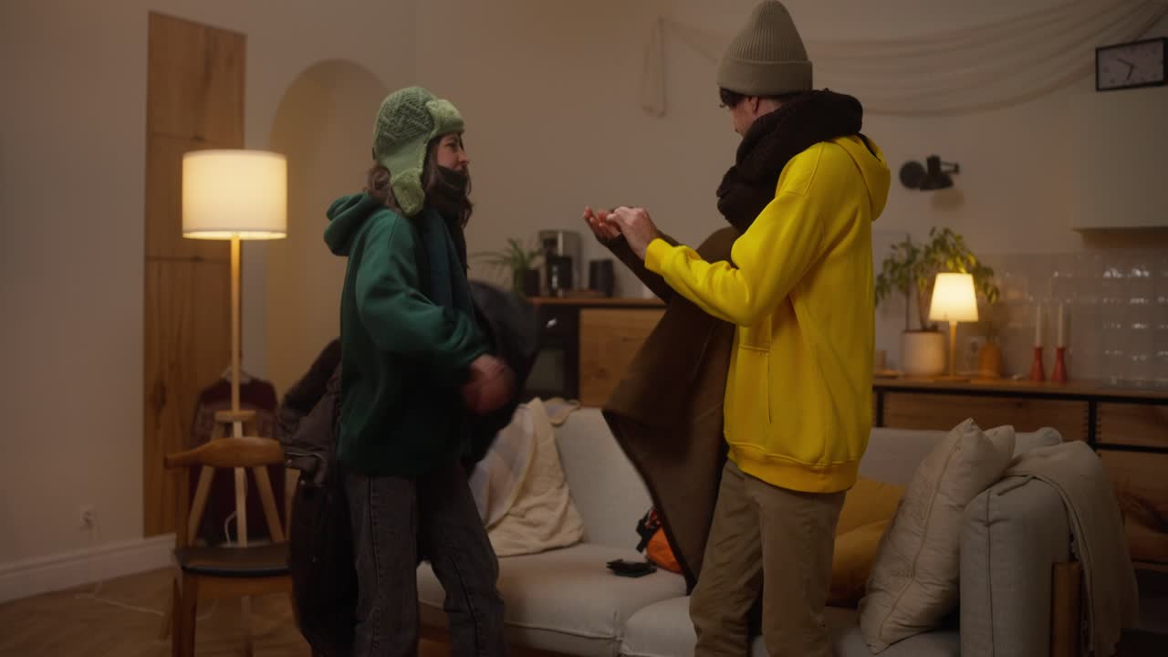 Couple playing with winter clothes in their living room at night