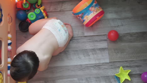 tiro de ángulo alto en cámara lenta de un lindo bebé asiático oriental de un año de edad aprendiendo a jugar con bolas rodantes en un patio interior en casa