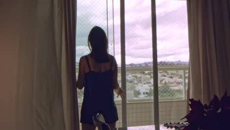 silhouette of brunette woman opening home balcony sliding doors in slow motion on a windy overcast day