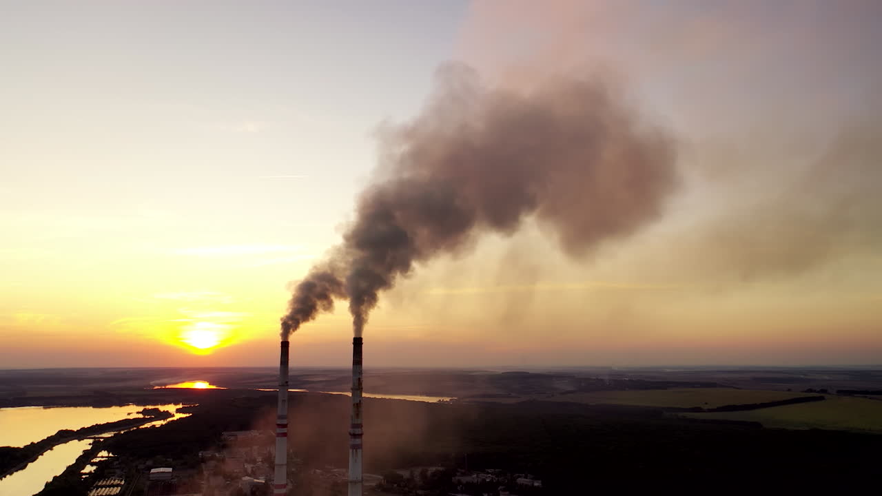 Environment pollution. Dark smoke going from two industrial pipes on nature background at sunset.