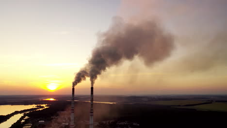 environment pollution. dark smoke going from two industrial pipes on nature background at sunset.
