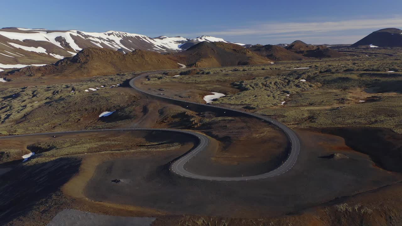 Winding Road By The Lava Field Overlooking The Icelandic Mountains Partly Covered In Snow During Summer In Iceland