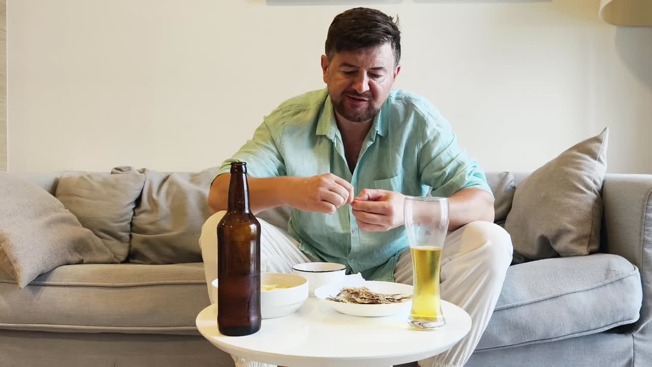 Man relaxing on a sofa, eating snacks and drinking beer