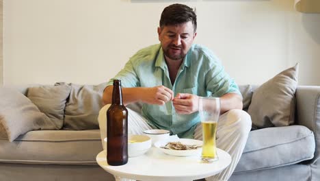 man relaxing on a sofa, eating snacks and drinking beer