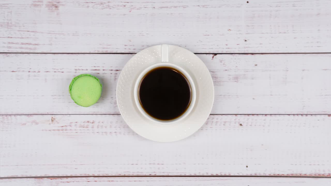 Stop motion of colorful macaroons and a cup of coffee on wooden background, close-up flat lay.