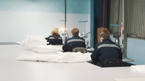 General-view-of-women-in-work-uniforms-sewing-white-fabric-on-factory-sewing-machines-in-a-textile-production-facility