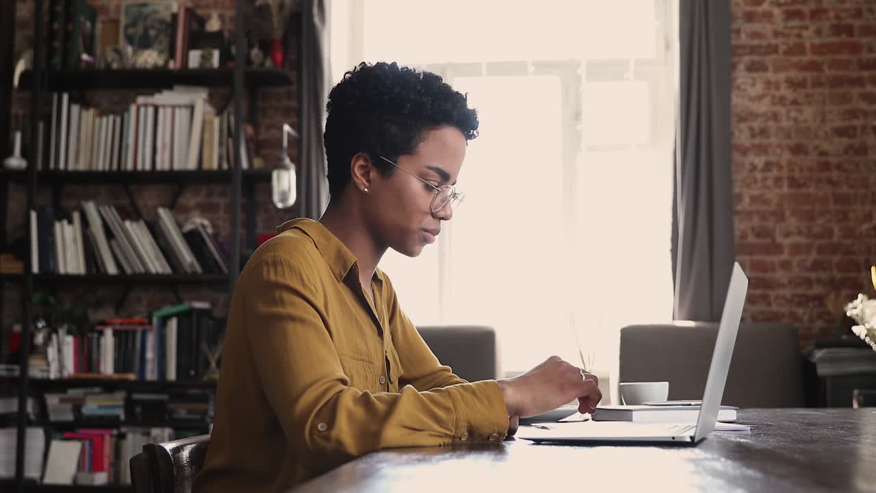 African woman sit at desk working on laptop, do paperwork