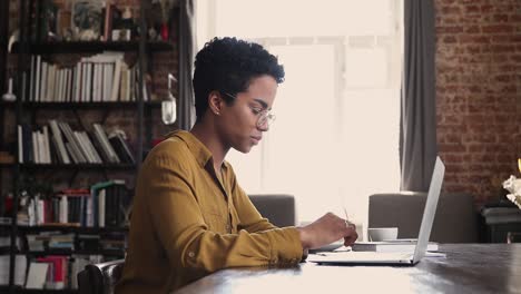 african woman sit at desk working on laptop, do paperwork