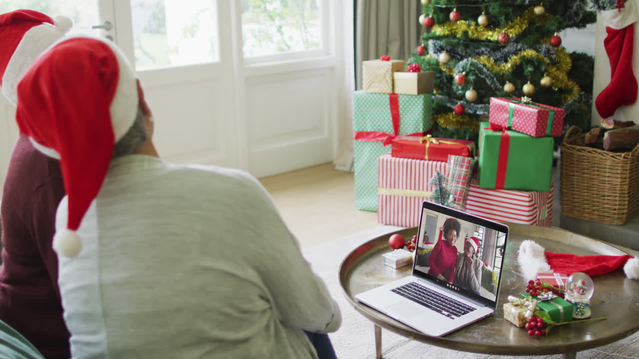 diversas amigas mayores que usan una computadora portátil para una videollamada de navidad con una familia sonriente en la pantalla