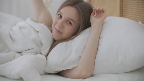 smiling woman waking up. teen hispanic woman wakes up at home. young girl stretching after awake starting a new day with energy and vitality on bed near window in bedroom at morning back view.