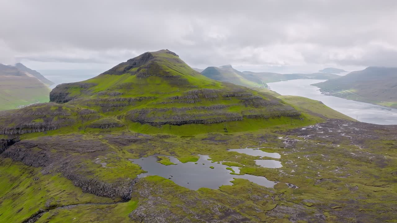 Green faroe islands mountain landscape with lakes and cloudy skies , aerial view