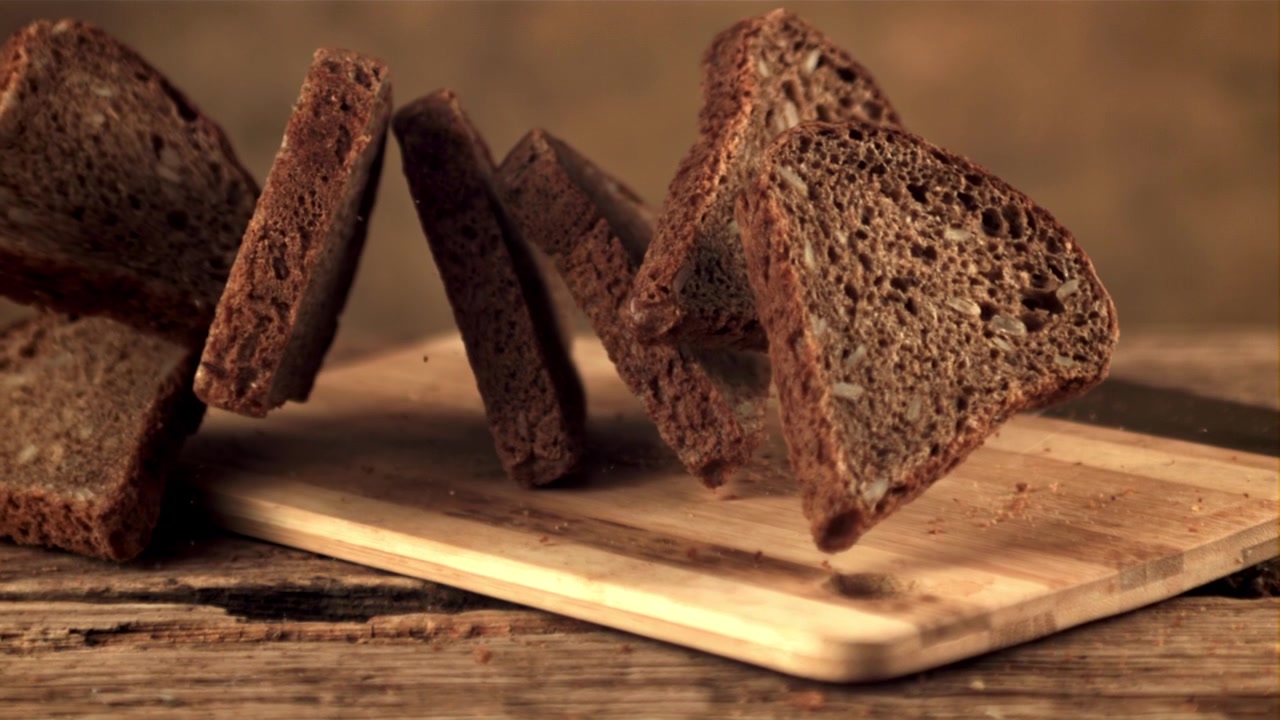 Slow Motion of Sliced Dark Bread Falling onto a Wooden Cutting Board