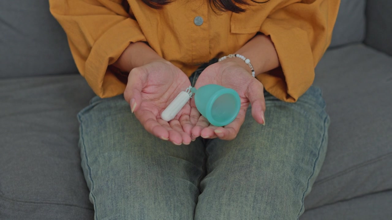 Reusable menstrual cup and white cotton tampon held in hands for feminine hygiene choice concept