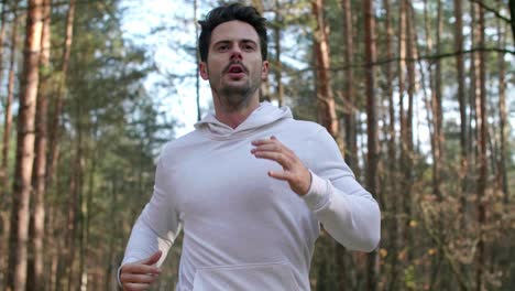 Front-view-of-young-man-running-in-the-forest