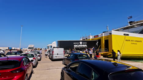 vehicles and passengers boarding a large yellow ferry at a bustling port