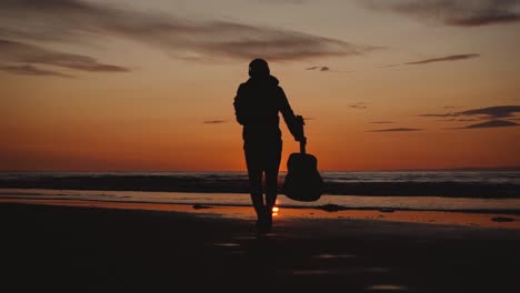 Mann-Läuft-Mit-Gitarre-Im-Hinteren-Sandstrand-Bei-Sonnenuntergang