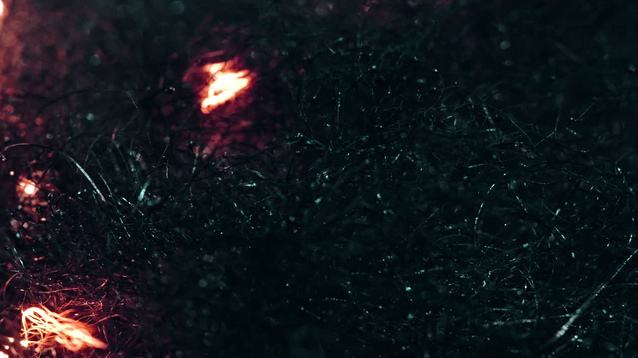 Burning embers slowly ignite dark fibrous material in a macro shot, creating a dramatic effect