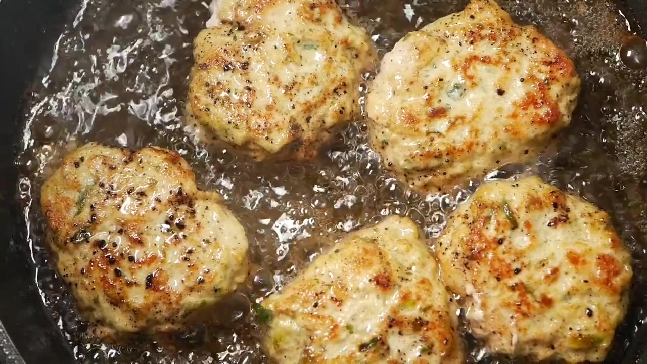 Four Seasoned Chicken Patties Frying in a Hot Skillet