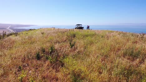 Steigende-Antenne-Eines-älteren-Rentners-Und-Einer-Frau,-Die-Neben-Einem-ATV-Am-Wunderschönen-Küstenblick-Auf-Den-Pazifik-Von-Gaviota-Und-Die-Grafschaft-Santa-Barbara-In-Kalifornien-Stehen