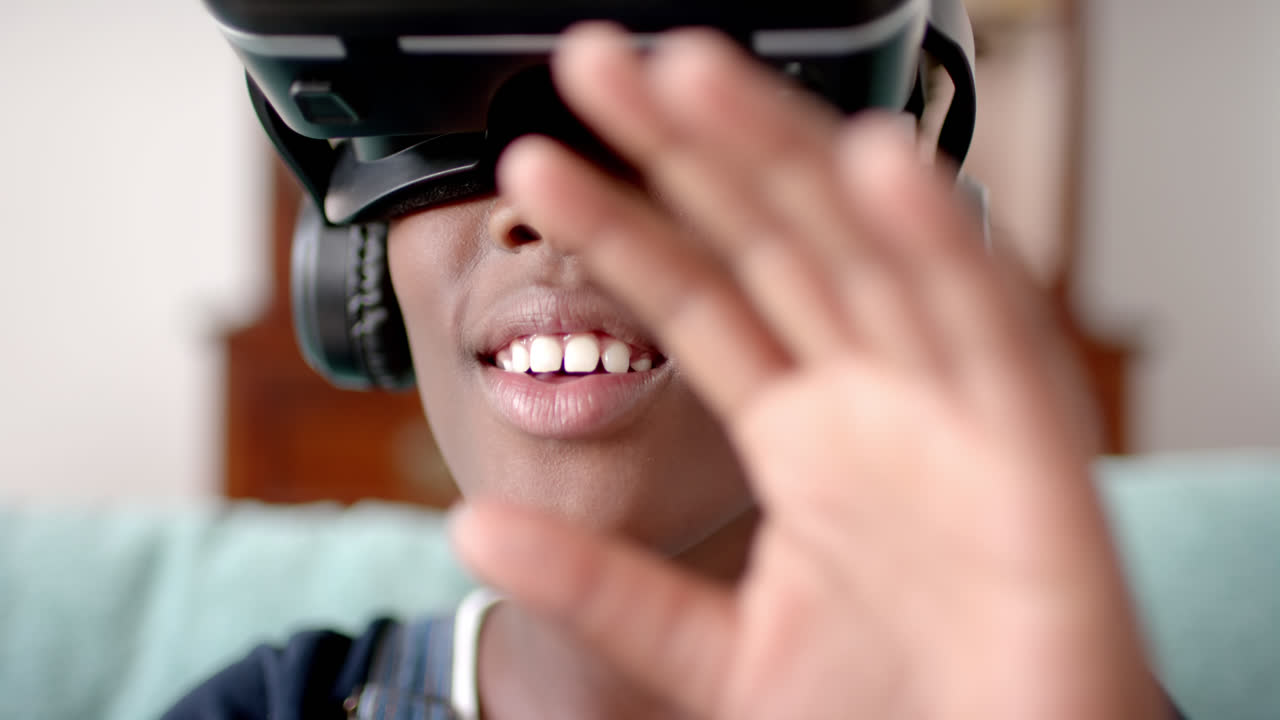 African american girl using vr headset and touching virtual screen in living room, slow motion