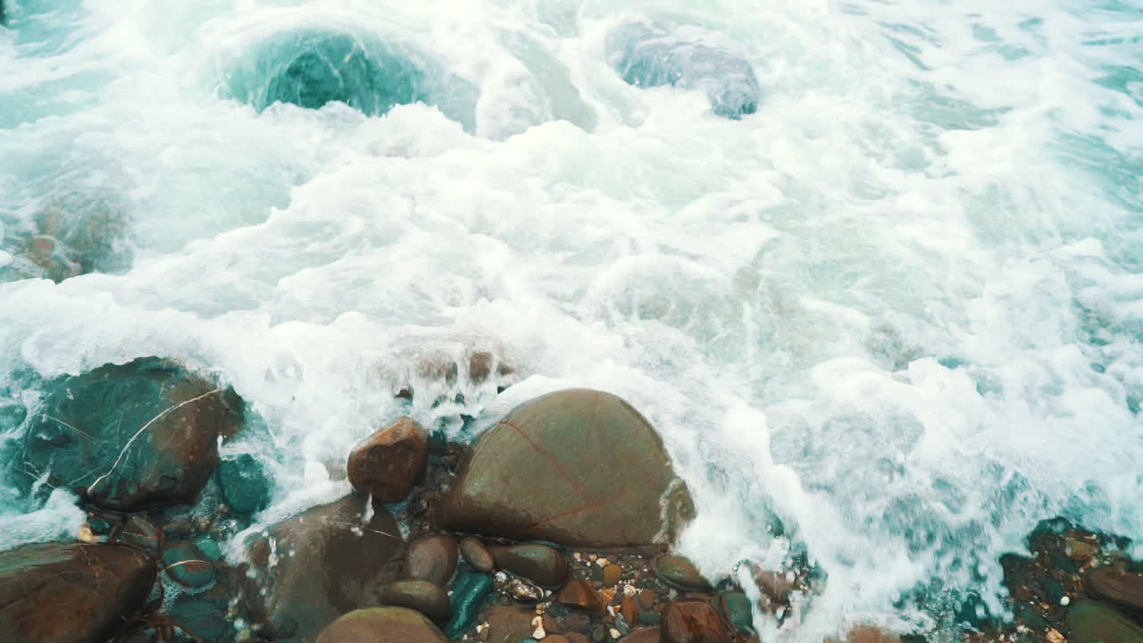 lavado blanco del océano y olas rompiendo lentamente sobre rocas y piedras en cornualles, inglaterra, cámara lenta de 120 fps