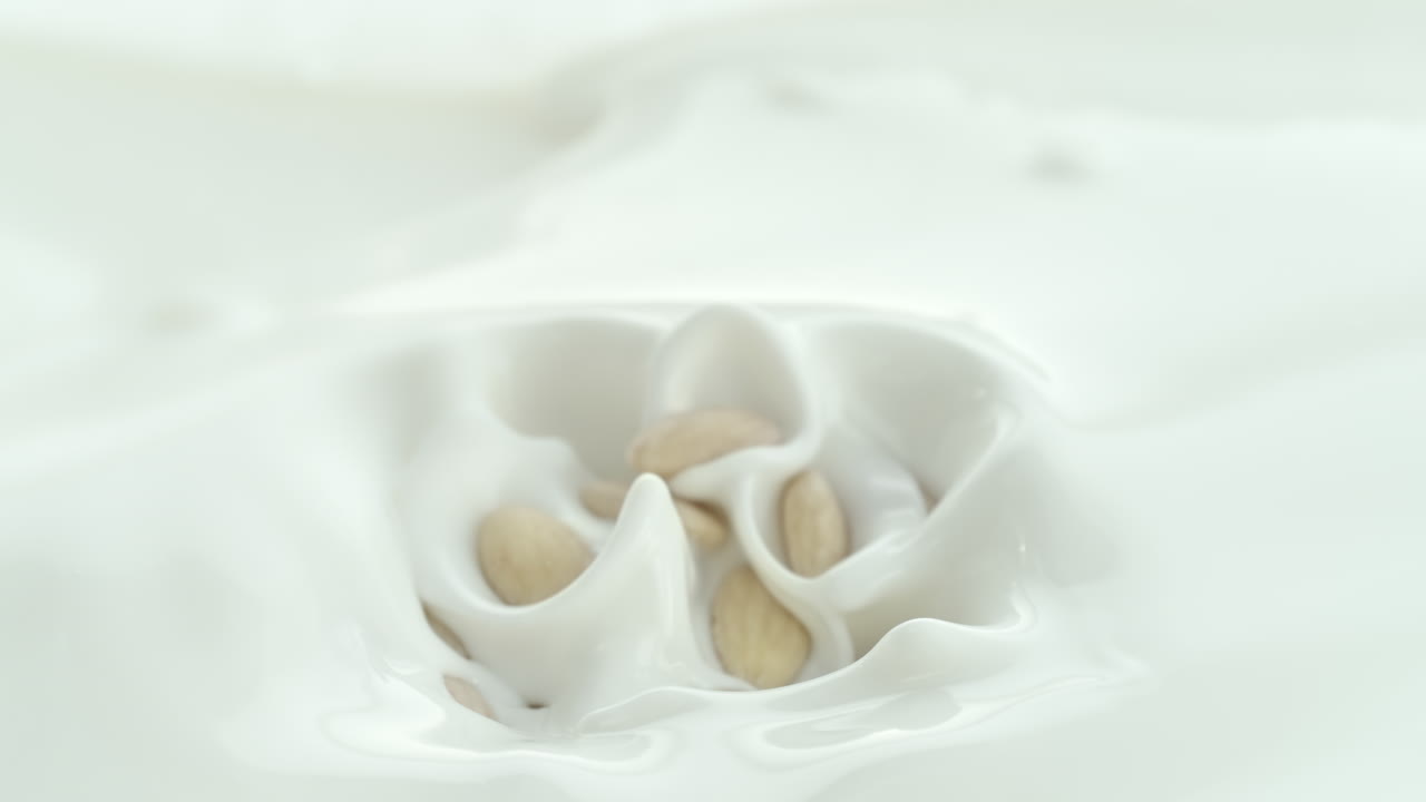 Blanched Almonds Falling into Creamy Milk Making Splash and Sinking in Macro and Slow Motion