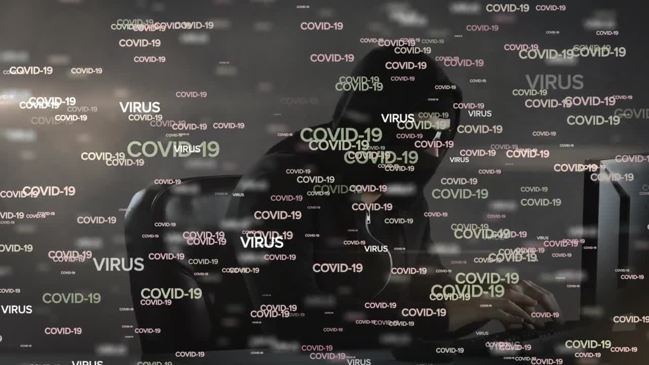 Animazione delle parole COVID-19 e VIRUS su un hacker incappucciato al computer.