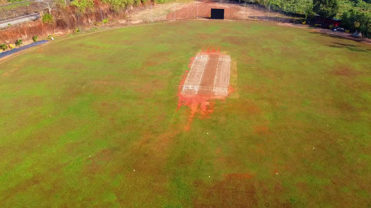 Luftfoto taget med drone af en frodig grøn cricketbane med en velholdt pitch og sight screen, perfekt til sport, rekreation og udendørs konkurrencetemaer.