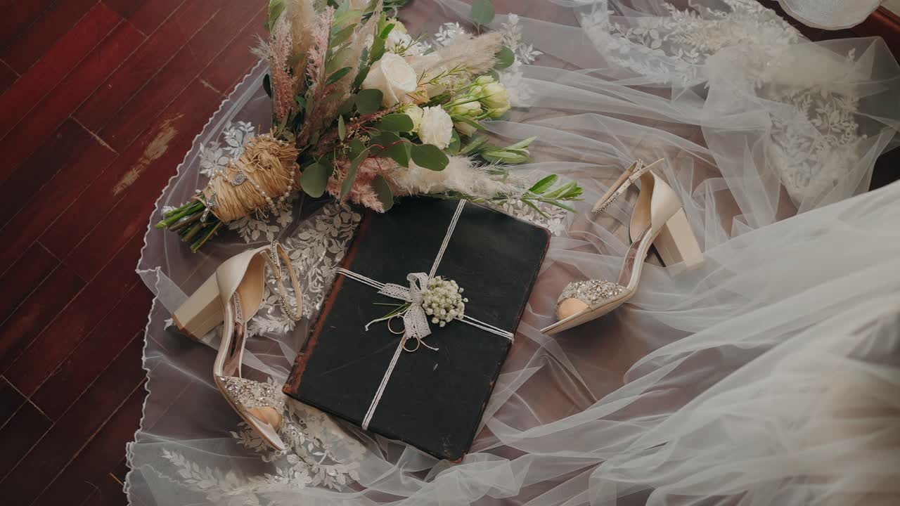 bridal bouquet, shoes, and a wrapped gift placed on a lace veil over a wooden floor