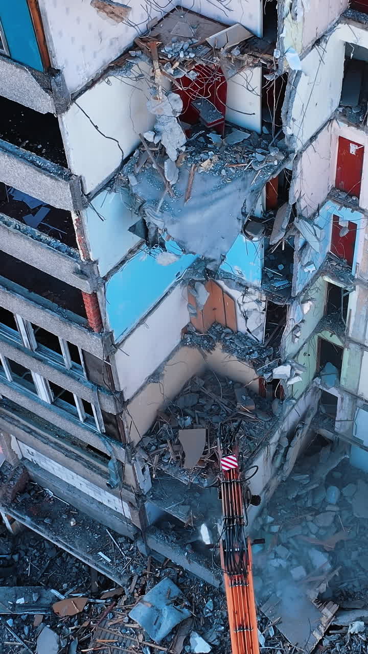Deconstruction of old premises with the excavator claw. Heavy machinery demolishing debris and turning it into dust. View from above. Vertical video