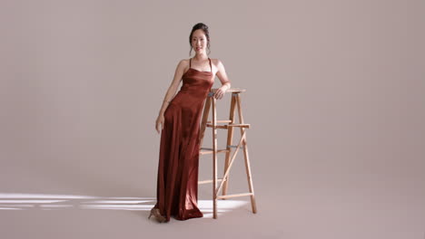 chinese female model entering studio, leaning on ladder, pivoting back, brushing cheek in light