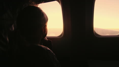 girl sitting in an airplane looking out the window at the rising sun