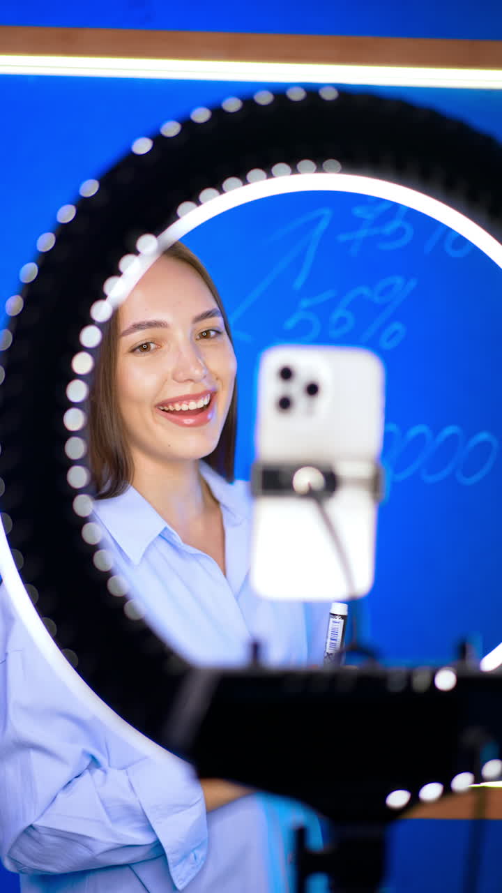 Beautiful smiling Caucasian brunette taking video with ring light. Modern blogger recording content. Vertical video.