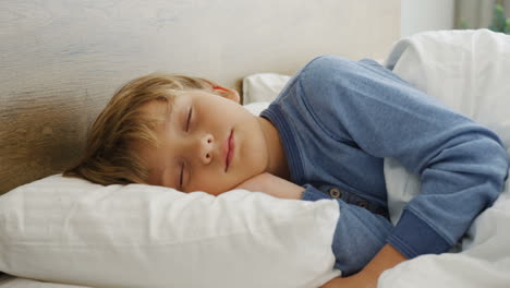 vista de cerca de un lindo niño rubio durmiendo en la cama por la mañana