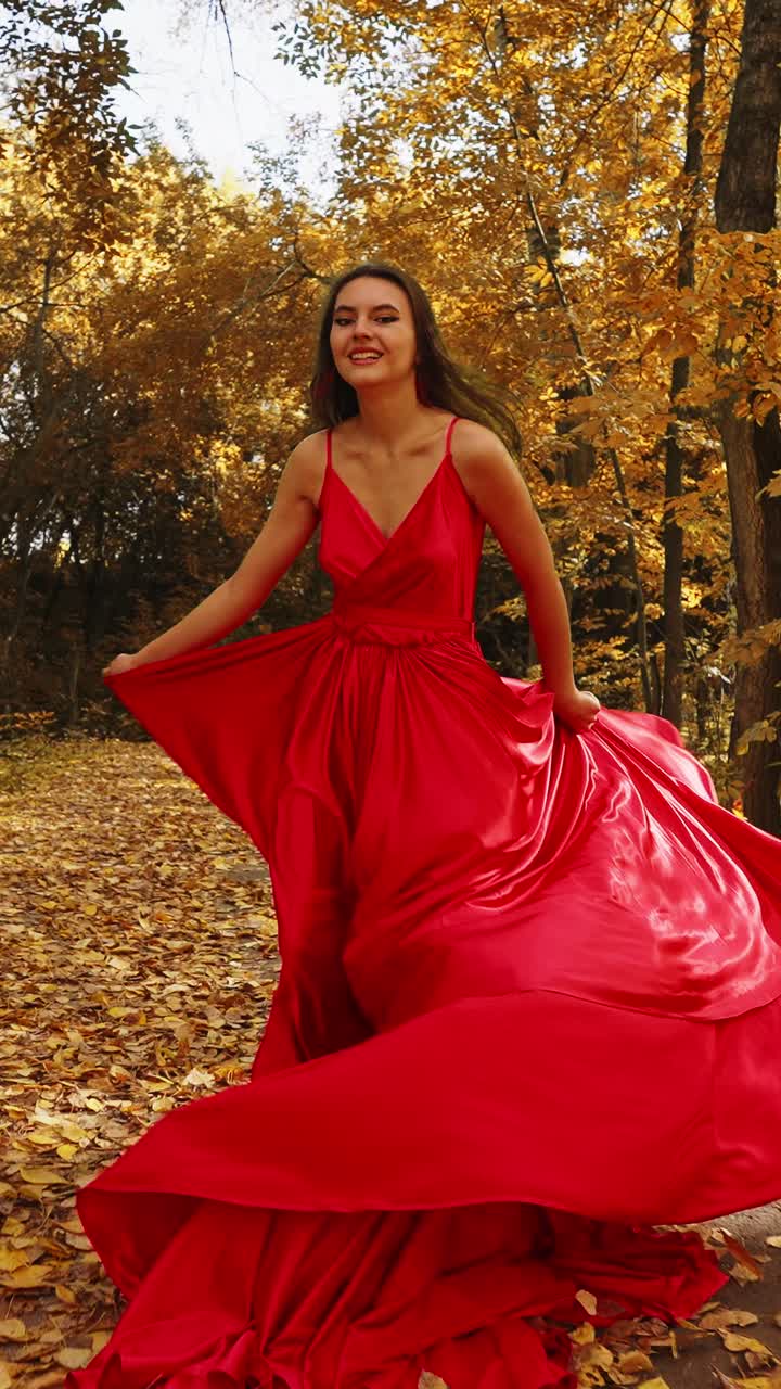Una donna con un abito rosso svolazzante passeggia in una foresta autunnale, ammirando con grazia ed eleganza i colori vivaci dell'autunno