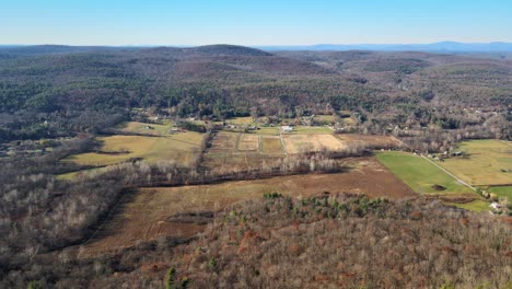 Aerial-side-pan-footage-of-farmland-as-seen-from-far-above-during-late-autumn-with-fields,-forests,-hills,-and-mountains