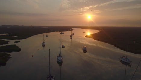 low cinematic drone shot of sailing boats on creek at high tide with birds flying past with reflections at stunning orange sunrise in wells-next-the-sea north norfolk uk east coast