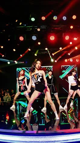 energetic kpop group performing a dynamic dance routine on a brightly lit stage, showcasing synchronized movements and vibrant costumes under colorful spotlights and in front of a large led screen
