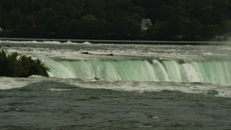 A breathtaking close-up shot of water cascading over the edge of Niagara Falls, shrouded in thick mist and backdropped by a lush forest