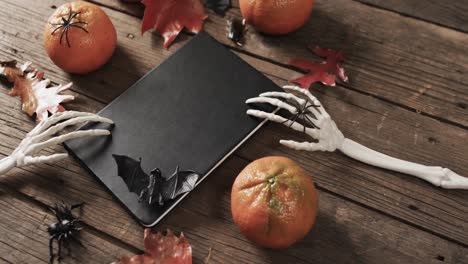 video of halloween skeleton hands, notebook and decorations with copy space on wooden background