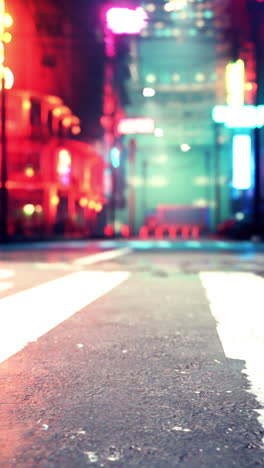 una vista borrosa de una calle de la ciudad por la noche, con luces de neón y un cruce peatonal en primer plano.