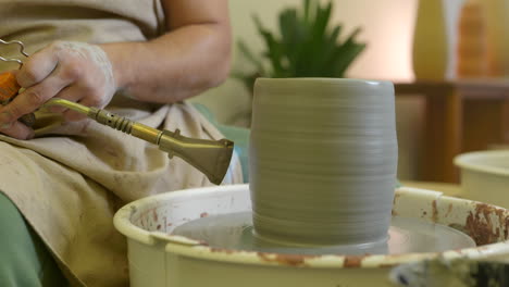 male hands using propane torch glazing clay pottery vase in studio workshop