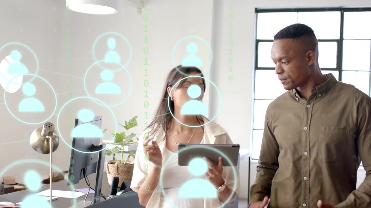 Woman tapping tablet and causing AR avatar overlay to grow as man gesturing reviewing business data