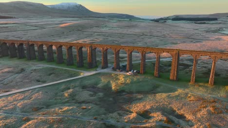 puente ferroviario con muchos arcos atrapando la luz del amanecer y las montañas de fondo llenas de nieve
