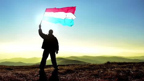 hombre ganador de silueta exitosa agitando la bandera de luxemburgo en la cima de la montaña, fondo de bucle de cinemagraph