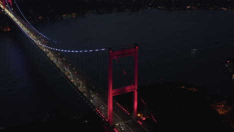 Red-Bosphorus-Bridge-in-Istanbul-at-Night-with-Car-traffic-into-the-City,-Establishing-Aerial-backwards-tilt-up