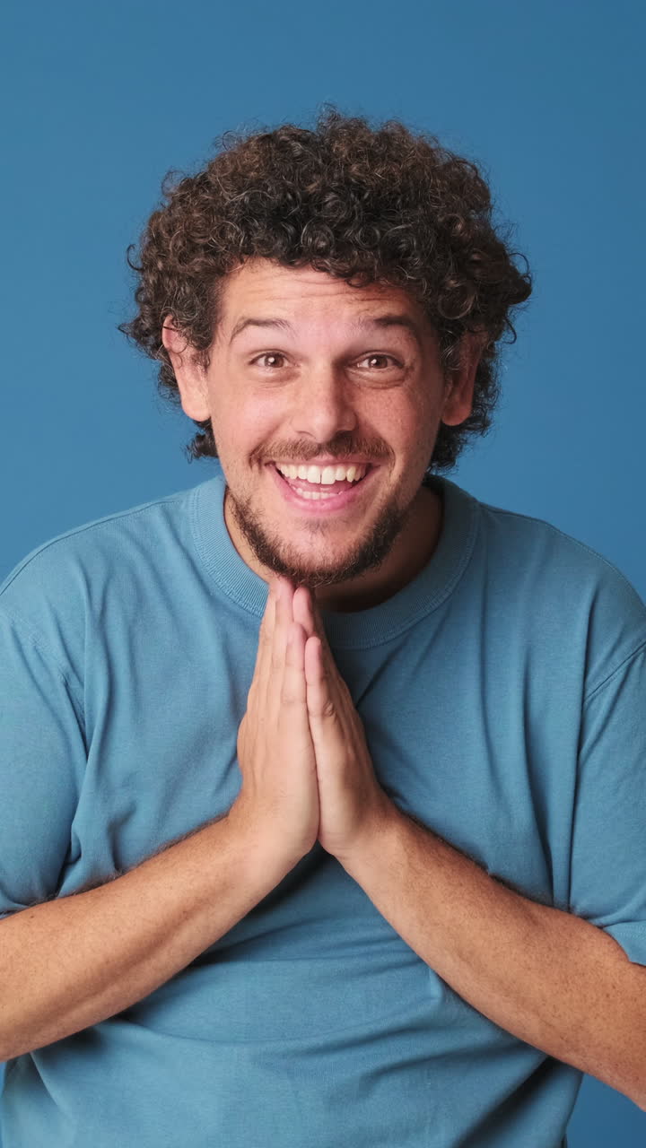 Hombre feliz muestra gratitud con las manos juntas sobre un fondo azul